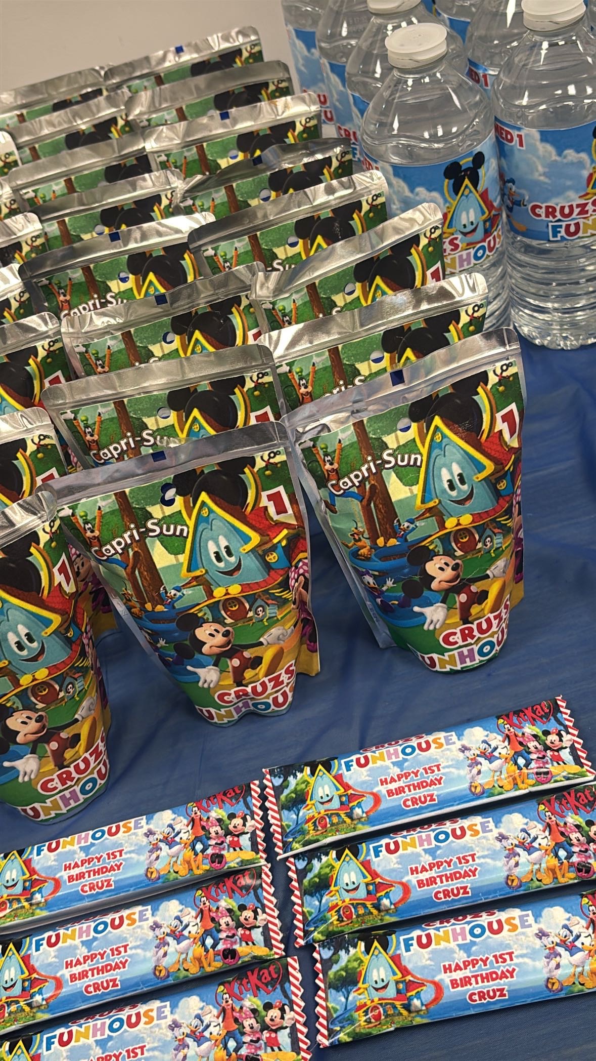 A colourful party table with personalised favour bags, water bottles and chocolate bars