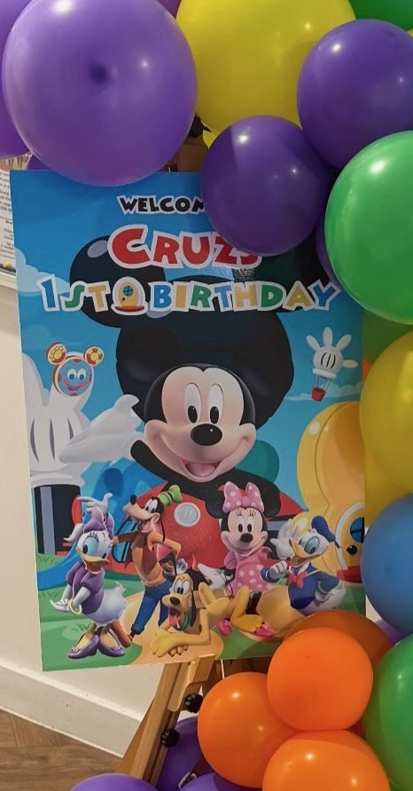 A personalised first birthday welcome sign framed by colourful balloons